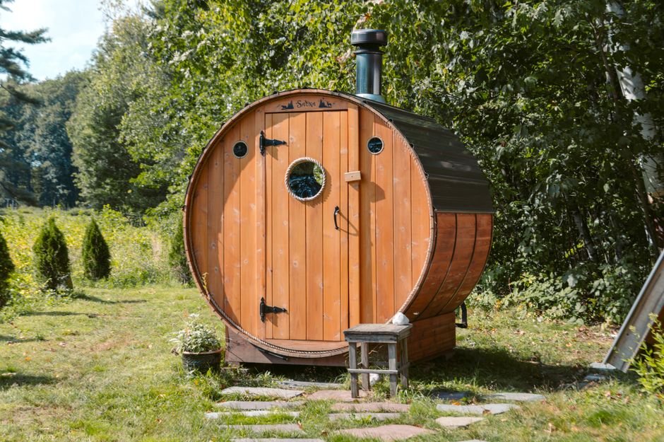 Wood-fired outdoor barrel sauna with a chimney in a green backyard