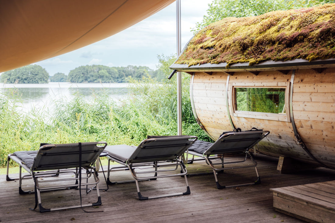 Outdoor barrel sauna beside a lake with lounge chairs