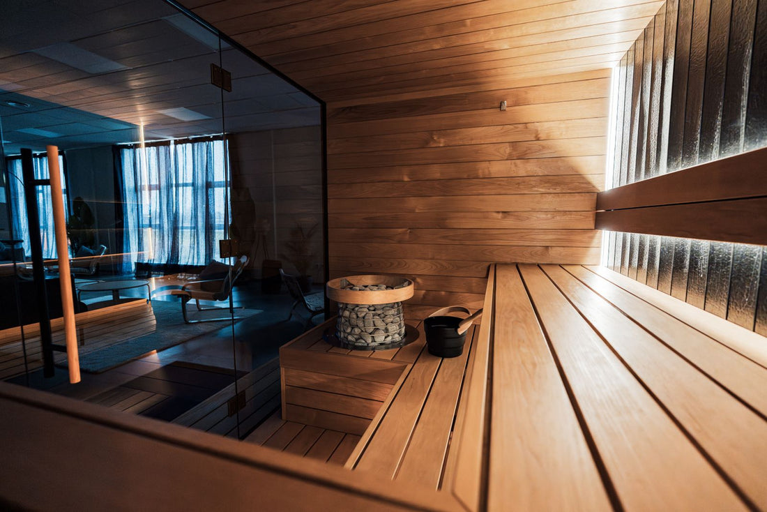 Modern cedar traditional sauna interior with wooden benches, a glass wall, and a stone heater
