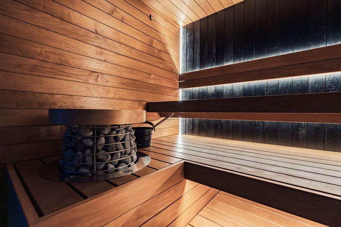 Traditional home sauna interior with an electric rock heater and cedar benches under LED lighting