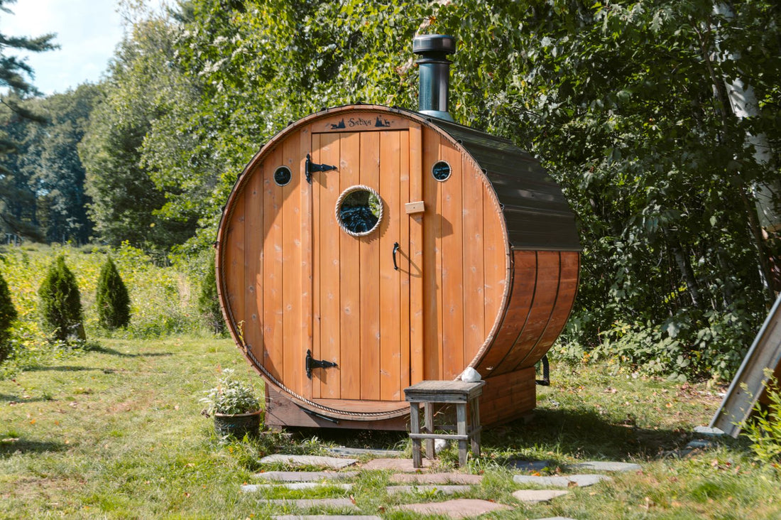 Outdoor barrel sauna with a round glass window and cedar staves in a green backyard