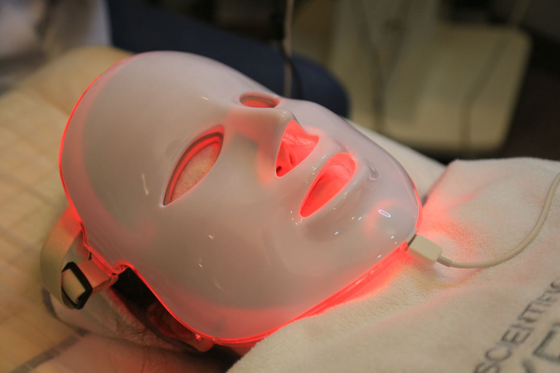 Red light therapy LED face mask glowing red during a session, one of the three device formats compared against panels and blankets