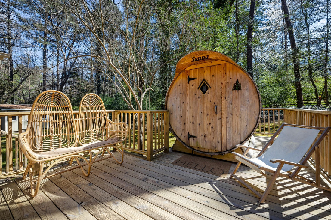 Cedar barrel sauna on a backyard deck surrounded by trees, with lounge seating