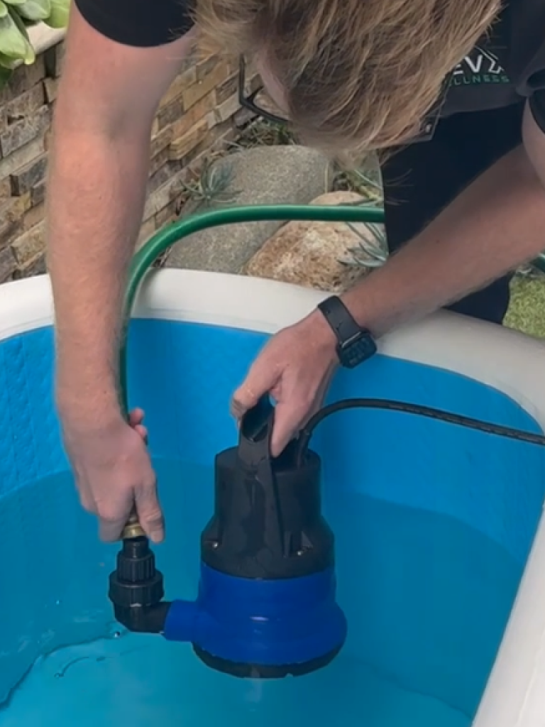 Person lowering the RevX drain pump into a cold plunge tub with the hose attached