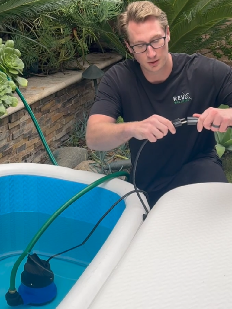 Person connecting the drain hose while the RevX pump sits in the tub
