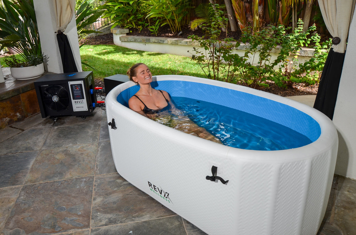 Person seated in a filled RevX Inflatable Deluxe on a patio with the chiller alongside