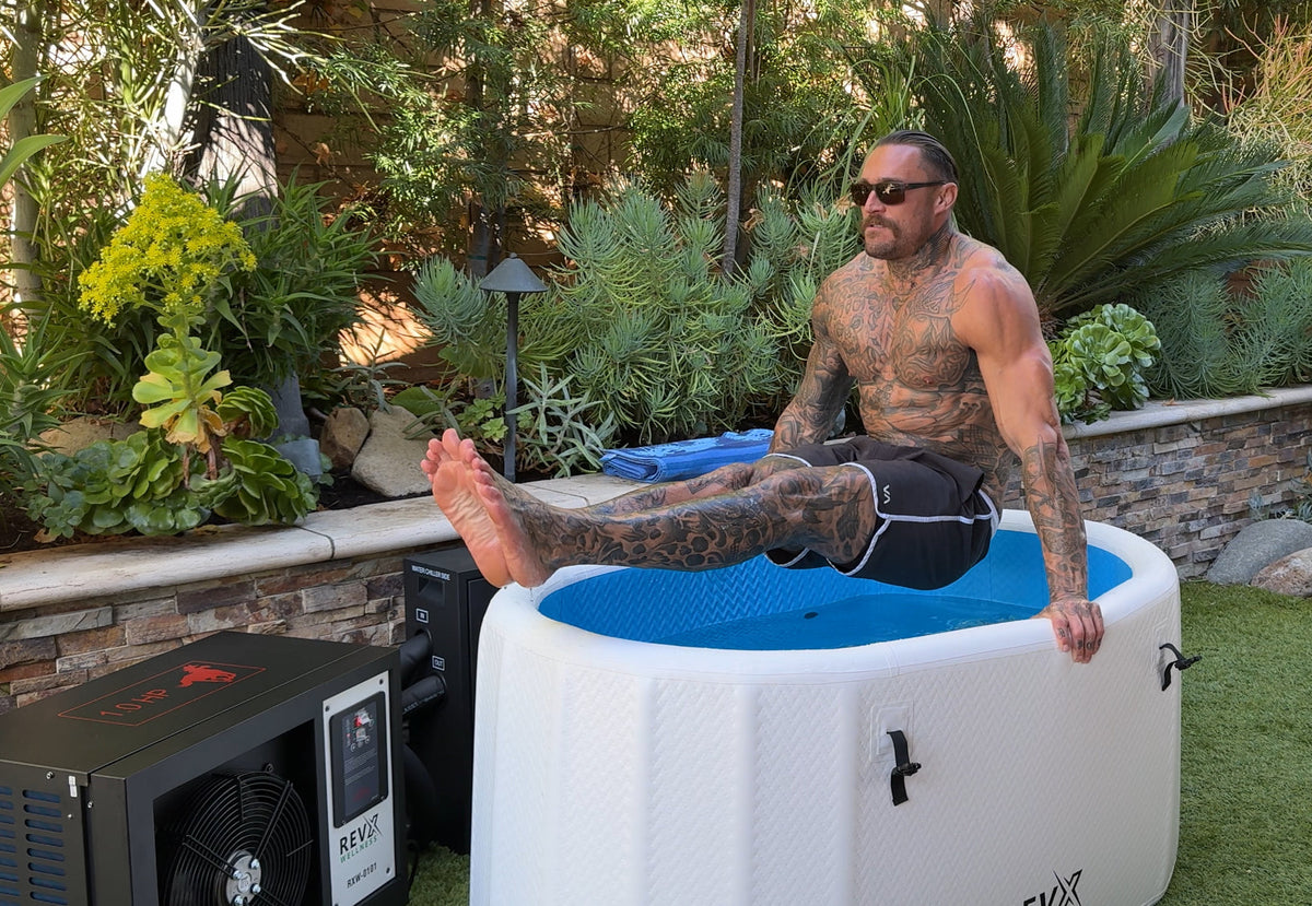 Person sitting on the edge of a filled RevX Inflatable Classic in a garden with the chiller behind