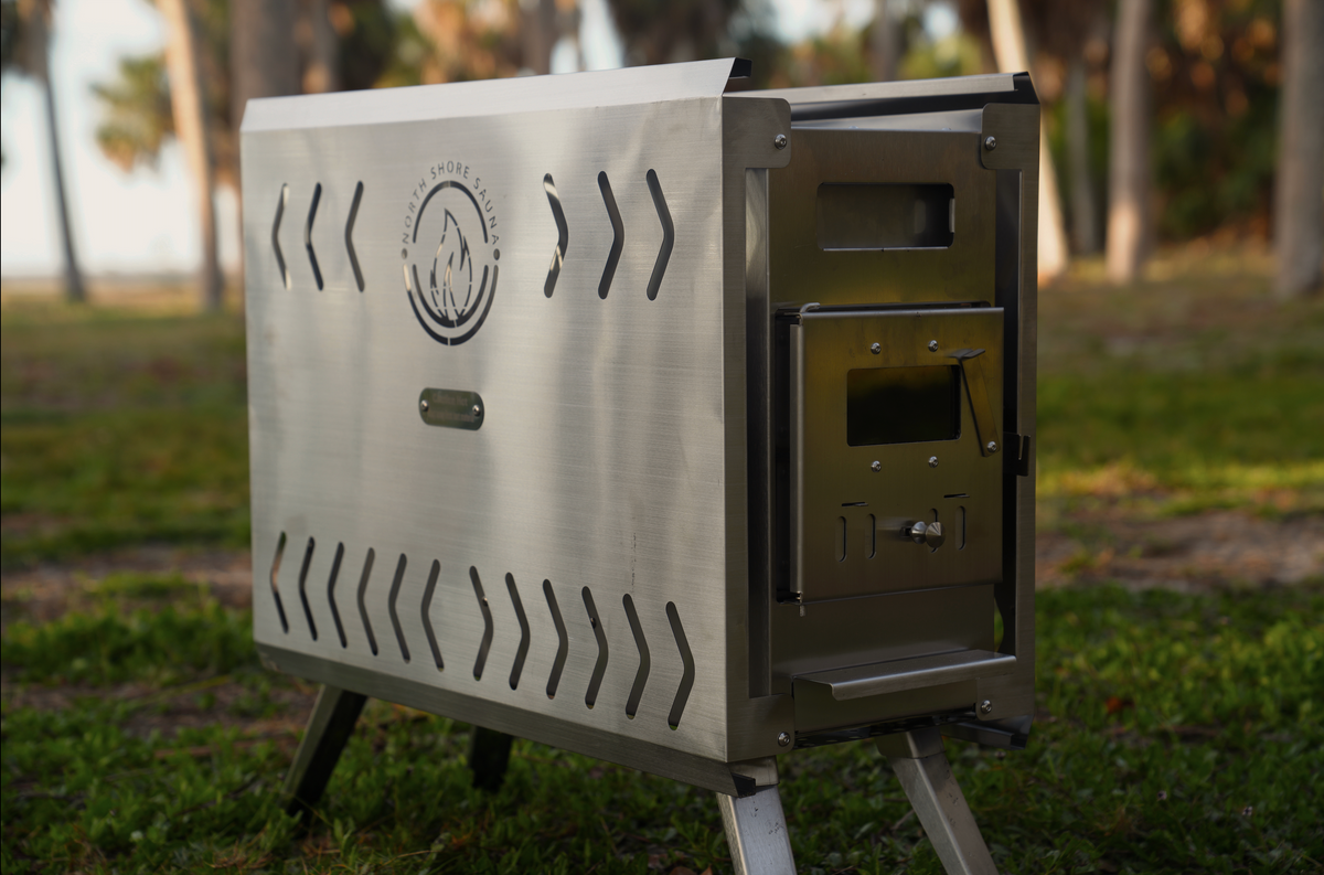 Brushed SS304 stainless steel portable sauna tent wood stove with chimney collar and folding legs, North Shore Sauna, shown outdoors