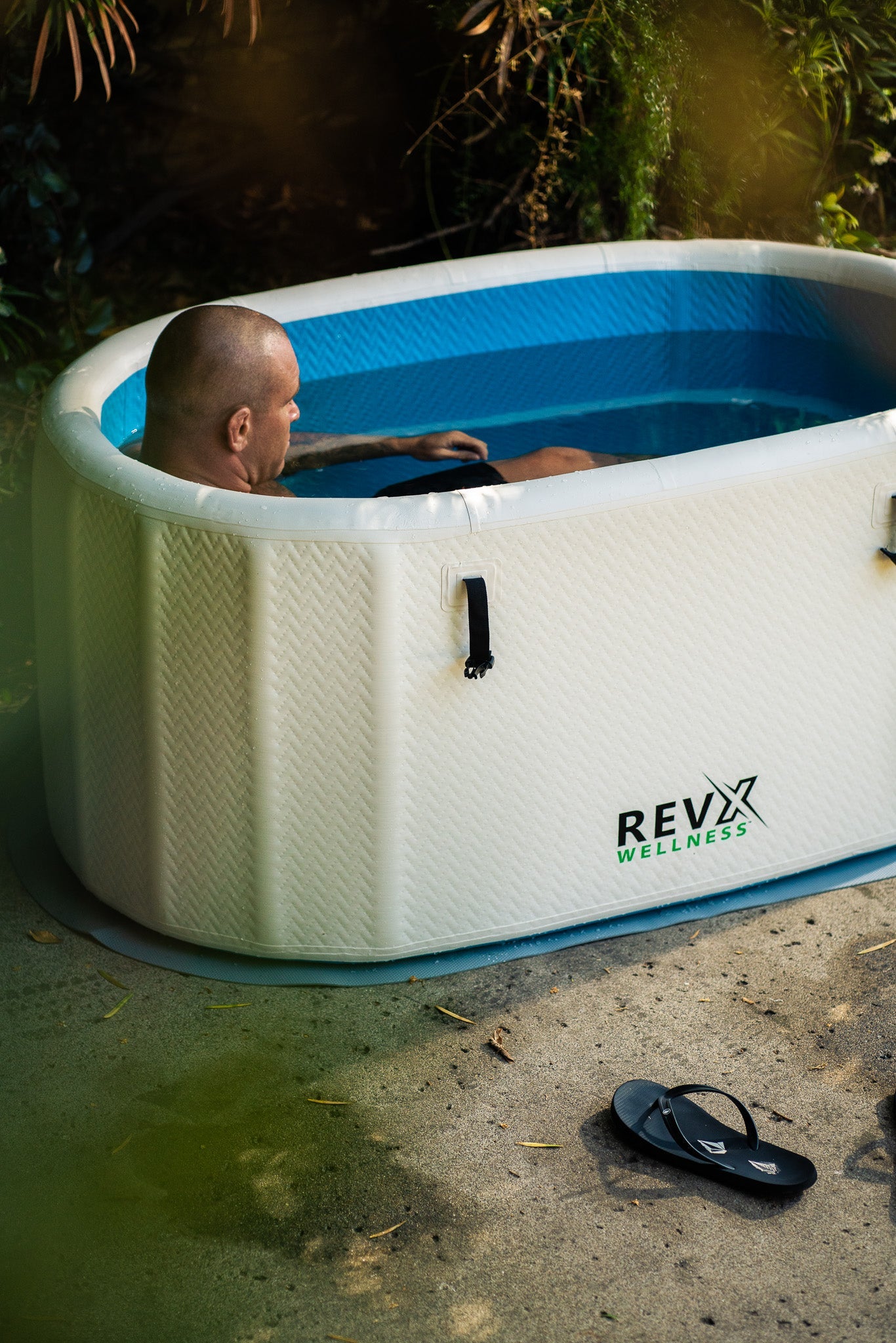 Person resting in a RevX Inflatable Classic cold plunge in an evening garden setting