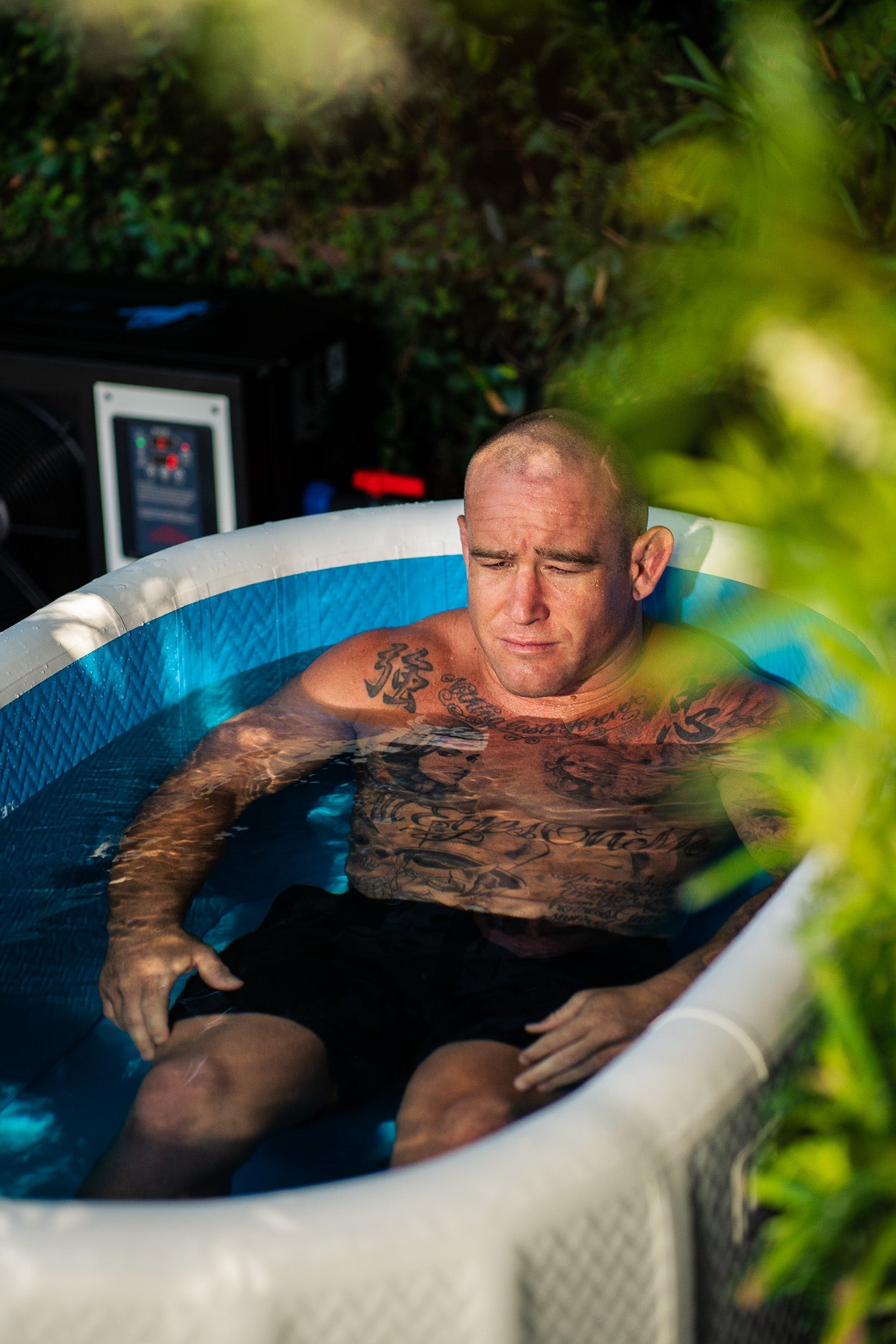 Person submerged in a RevX Inflatable Deluxe cold plunge outdoors beside the chiller