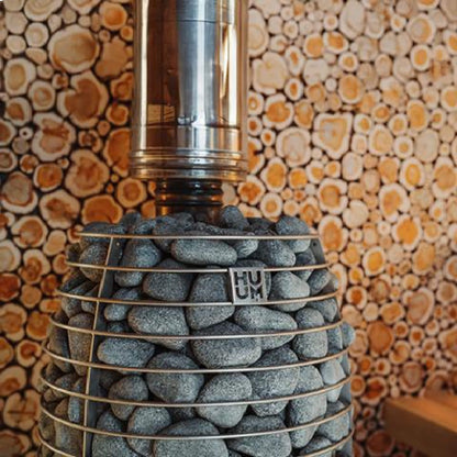 Huum Hive Flow Mini stove and steel chimney against a stacked log wall