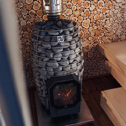 Huum Hive Flow Mini stove lit in a sauna beside a stacked log wall